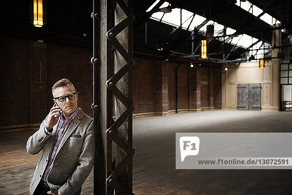 Businessman talking on smart phone while standing in empty warehouse