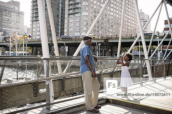 Enkelin fotografiert Großvater  während sie am Geländer einer Brücke in der Stadt steht