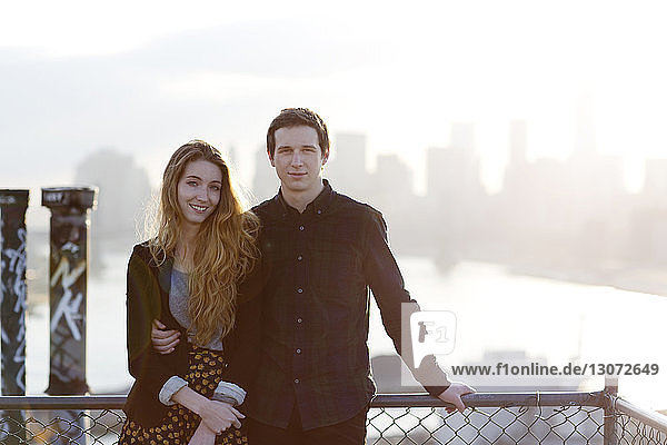 Portrait of couple standing by railing of tarries against city