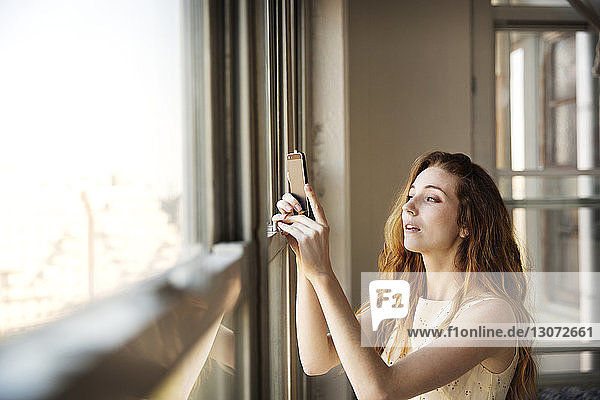 Woman photographing while standing by window at home