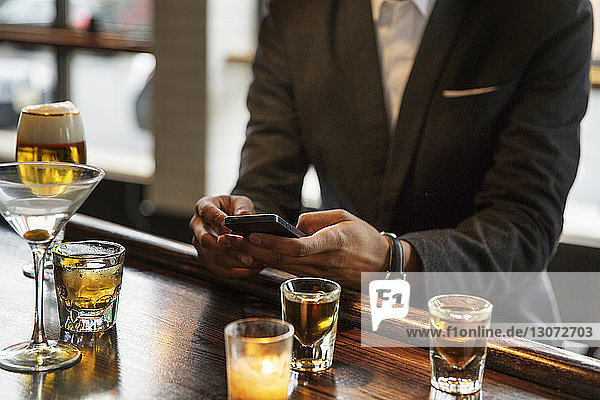Mittelsektion eines Mannes  der ein Smartphone benutzt  während er in einer Bar sitzt