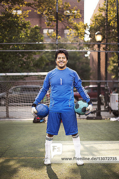 Porträt eines glücklichen Fußballspielers  der Bälle trägt  während er auf dem Spielfeld steht