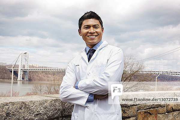 Portrait of happy doctor standing against bridge