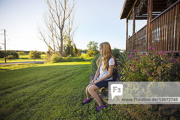 Thoughtful schoolgirl sitting on stones at yard