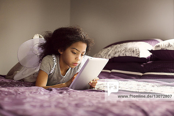 Mädchen in Feenflügeln benutzt Tablet-Computer im Schlafzimmer zu Hause