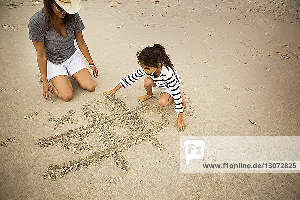 High angle view of mother and daughter playing tic-tac-toe on sand at beach