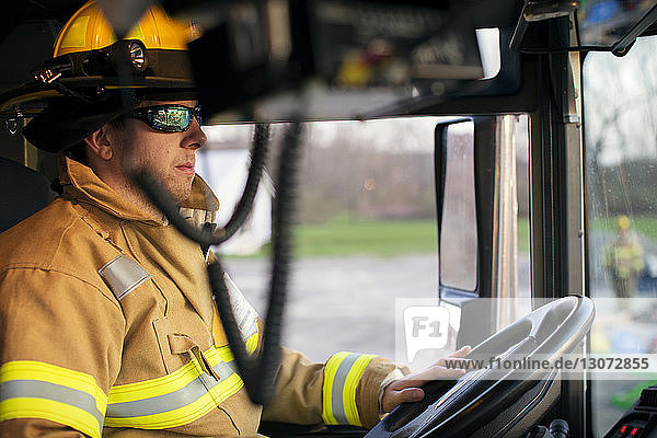 Selbstbewusster Feuerwehrmann schaut weg  während er im Feuerwehrauto sitzt