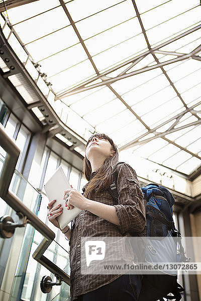 Niedrigwinkelansicht einer Frau mit Tablet-Computer  die im Bahnhof stehend nach oben schaut