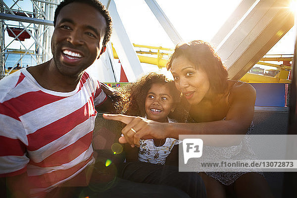 Frau mit Familie  die auf eine Fahrattraktion im Vergnügungspark zeigt