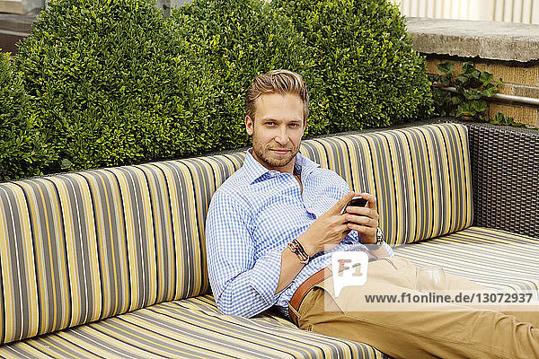 Porträt eines Mannes  der ein Smartphone in der Hand hält  während er auf dem Sofa sitzt