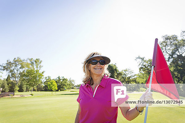 Portrait of happy woman holding flag while standing at golf course against clear sky