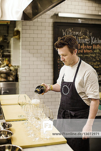 Mann gießt Wein in Gläser ein  während er in einer Großküche steht