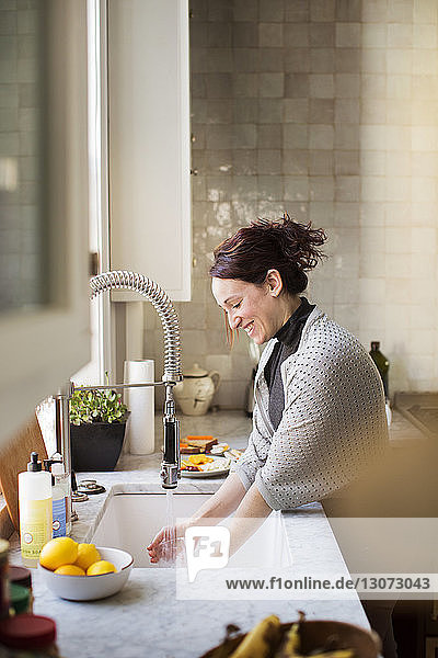 Seitenansicht einer Frau  die zu Hause Utensilien wäscht