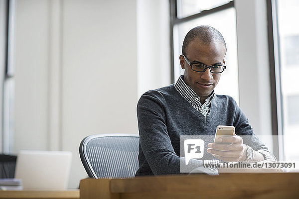 Geschäftsmann benutzt ein Smartphone  während er im Büro am Schreibtisch sitzt