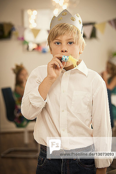 Portrait of boy blowing party horn blower while standing at home