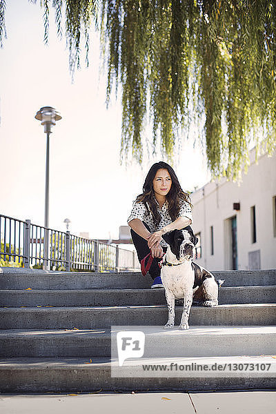 Frau sitzt mit Hund auf Stufen gegen den klaren Himmel