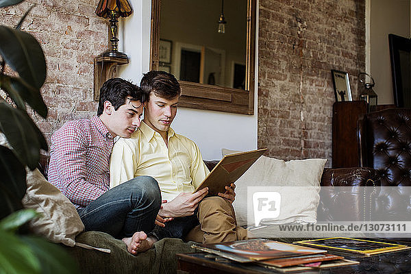 Schwules Paar hält Plattencover  während es zu Hause auf dem Sofa sitzt