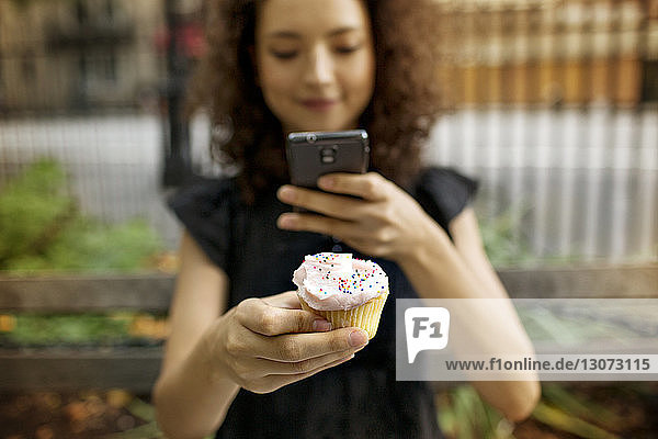 Frau fotografiert Cupcake  während sie im Straßencafé sitzt