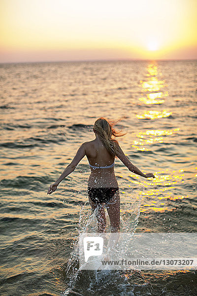 Rückansicht einer Frau  die bei Sonnenuntergang am Strand an der Küste läuft