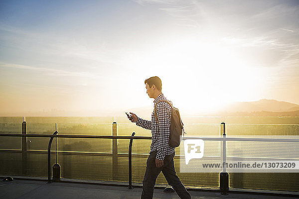 Side view of man using smart phone while walking by railing