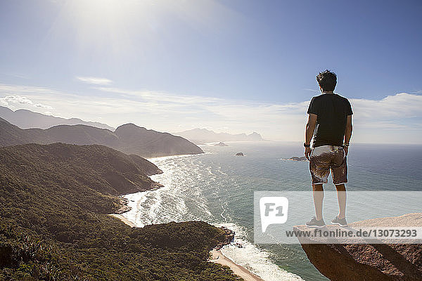 Rear view of hiker standing cliff by sea