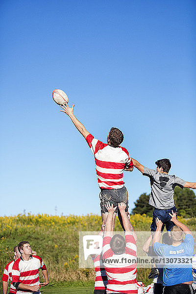 Rugby players catching ball against clear blue sky