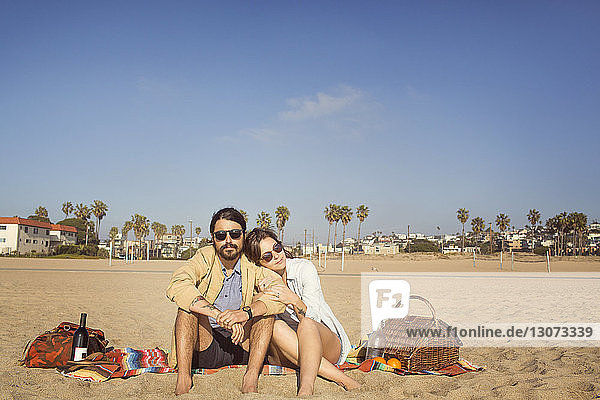 Couple relaxing at beach against blue sky on sunny day