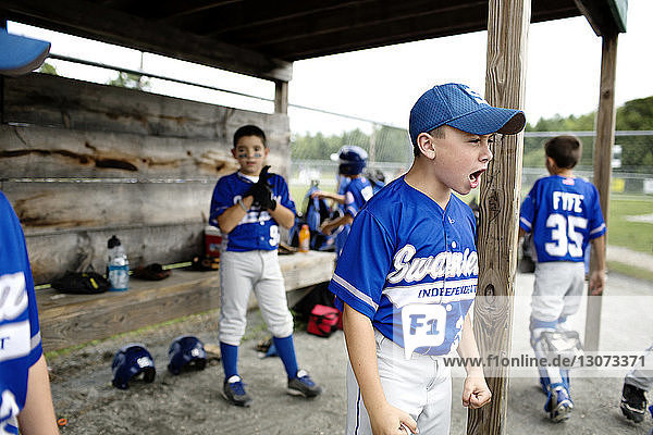 Boy shouting while standing with friend in dugout