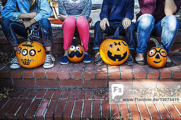 Niedriger Teil der Familie sitzt an Halloween mit dekorierten Kürbissen auf der Treppe