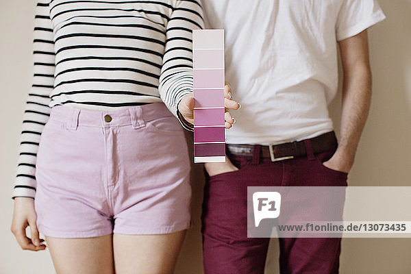 Midsection of woman holding color swatch while standing with man against wall at home
