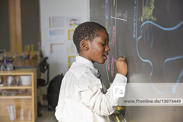 Side view of boy drawing on blackboard during lesson in classroom
