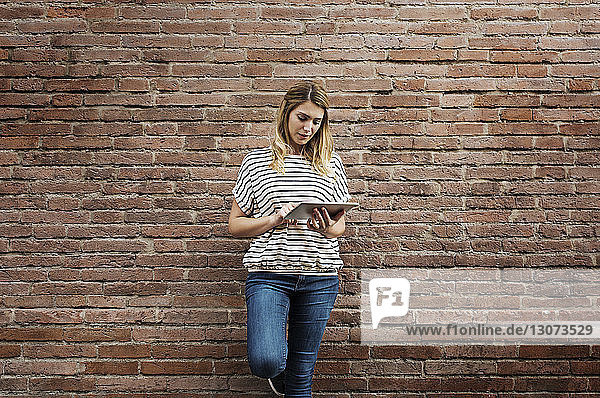 Woman using tablet computer while standing against brick wall