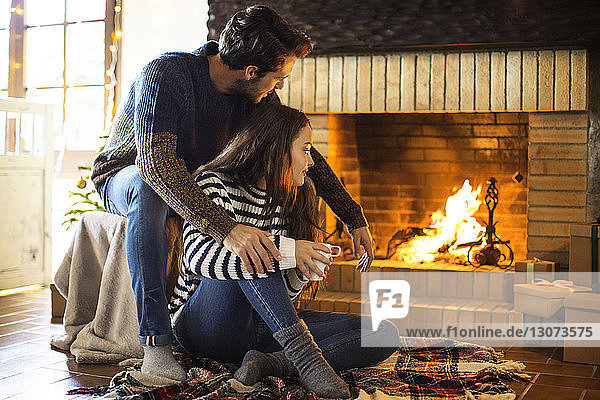Paar mit Kaffeetasse  das auf den Kamin schaut  während es auf dem Boden sitzt
