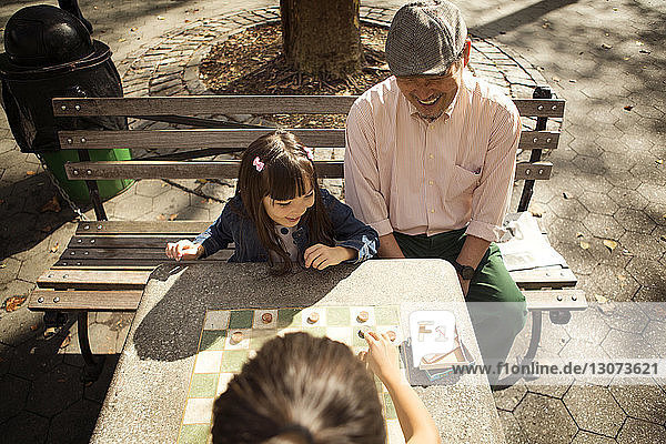 Hochwinkelansicht eines Großvaters  der Mädchen beim Damespiel im Park beobachtet