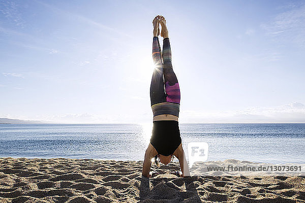 Young woman doing handstand on shore at beach