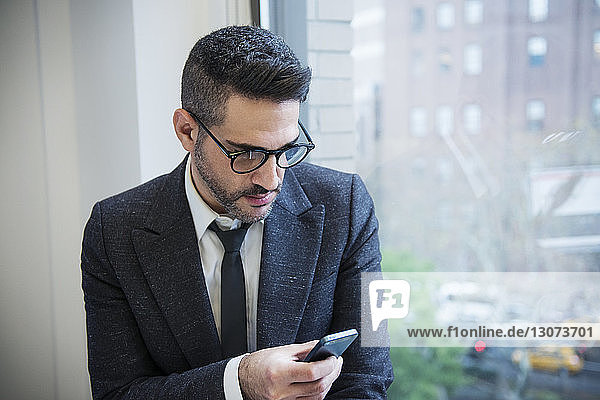Businessman using phone by window in office