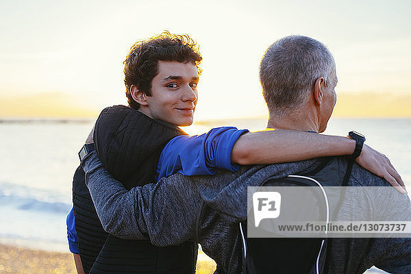 Portrait of confident son with arm around father's shoulder at beach
