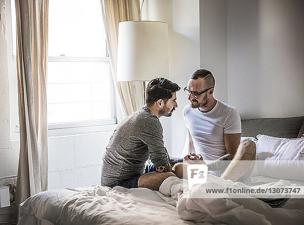 Homosexuelle Männer  die zu Hause auf dem Bett sitzen und Händchen halten