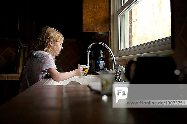 Girl filling cup with water in kitchen