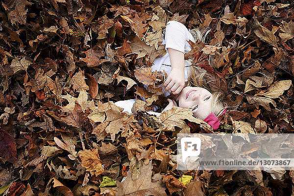 Hochwinkelaufnahme eines fröhlichen Mädchens  das im Herbst im Ahornblatt liegt