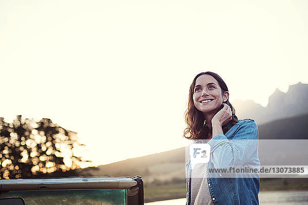 Woman looking away while standing by convertible car against clear sky during sunset