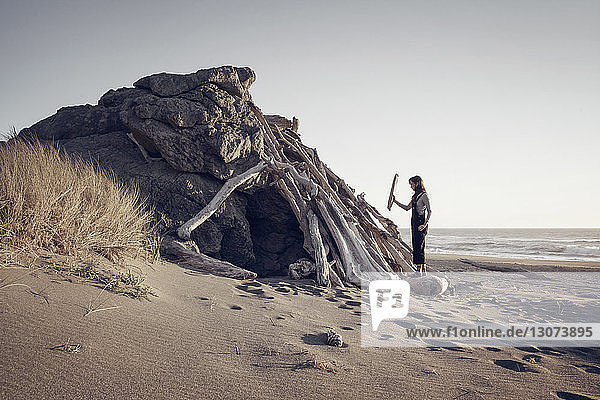 Frau arrangiert Holz auf einer Felsformation am Strand bei klarem Himmel