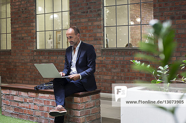 Geschäftsmann benutzt Laptop-Computer  während er auf einem Sitz vor einem Bürogebäude sitzt