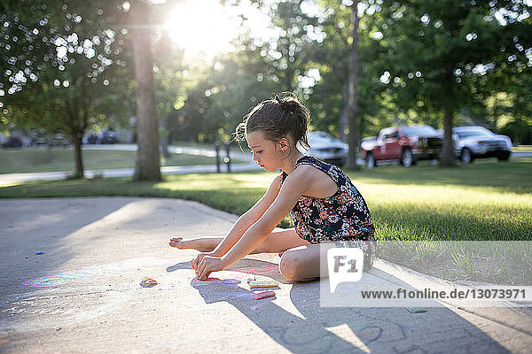 Side view of girl drawing with chalks on footpath at yard