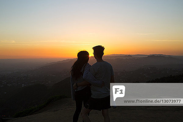 Rückansicht eines Paares  das bei Sonnenuntergang auf einem Berg gegen den Himmel steht