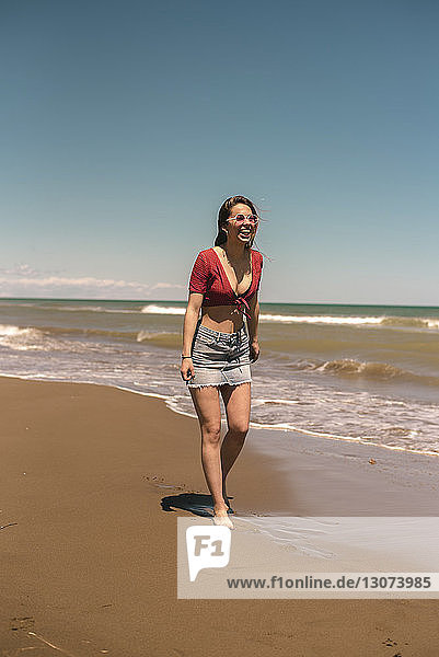Happy woman walking at beach against blue sky during sunny day
