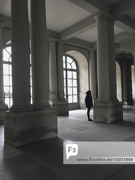 Frau steht in voller Länge an architektonischen Säulen in einem historischen Gebäude