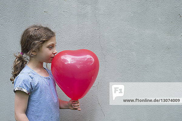 Side view of girl looking away while holding balloon against wall