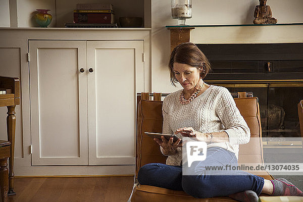 Frau benutzt Tablet-Computer  während sie auf einem Stuhl im Wohnzimmer sitzt