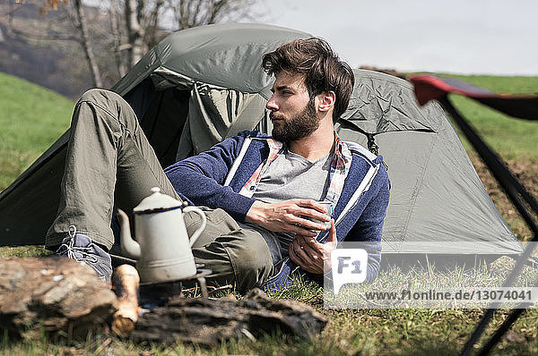 Nachdenklicher Mann entspannt sich vor dem Zelt auf dem Hügel
